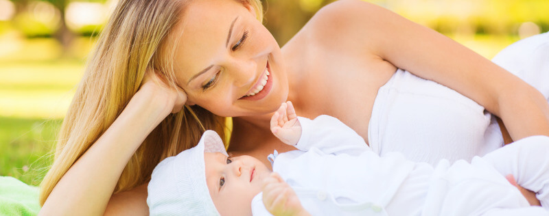 happy mother lying with little baby on blanket